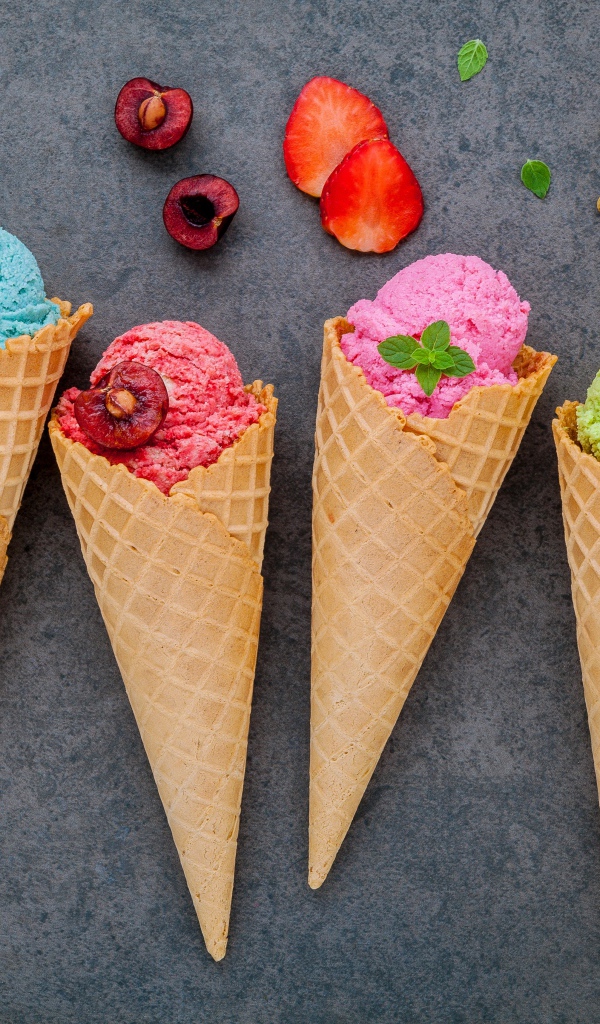 Шарики фруктового мороженого в вафельных рожках на сером фоне