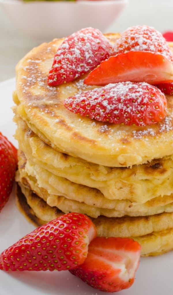 Оладьи с клубникой и сахарной пудрой на белой тарелке 