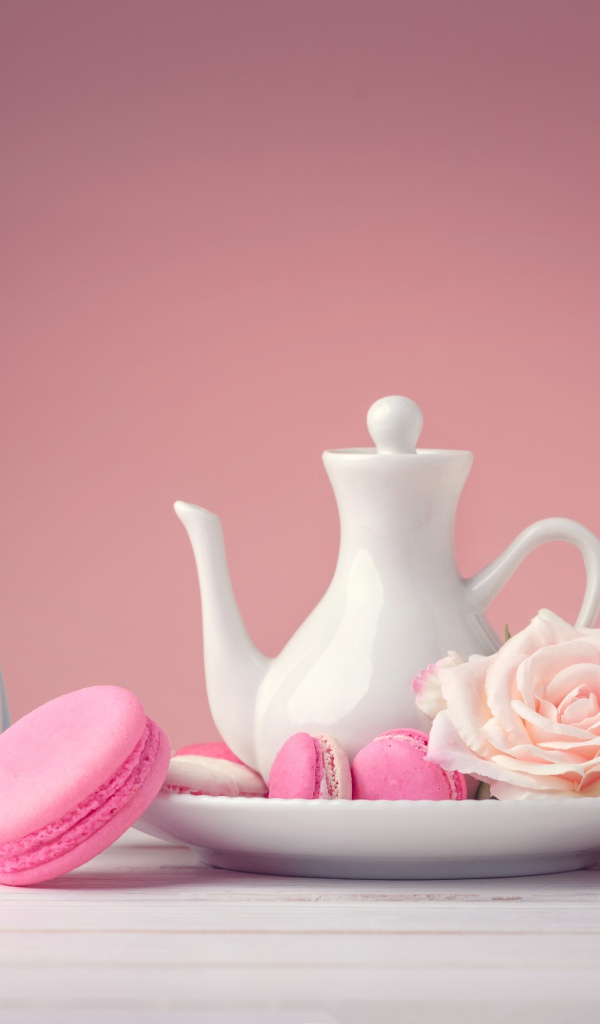 Розовый десерт макарун на столе с белый чайником и цветами розы