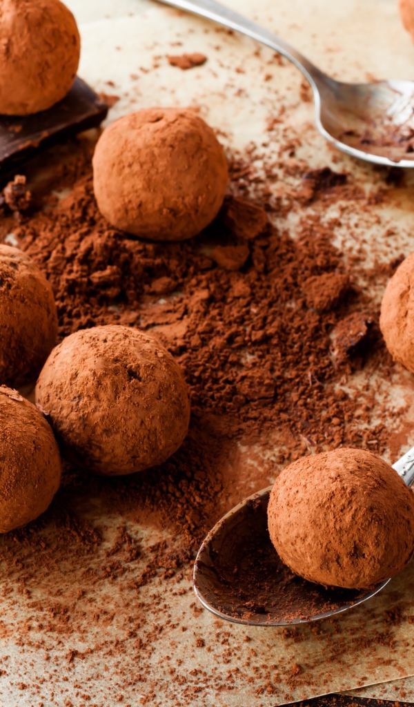 Круглые шоколадные конфеты в какао на столе с ложками