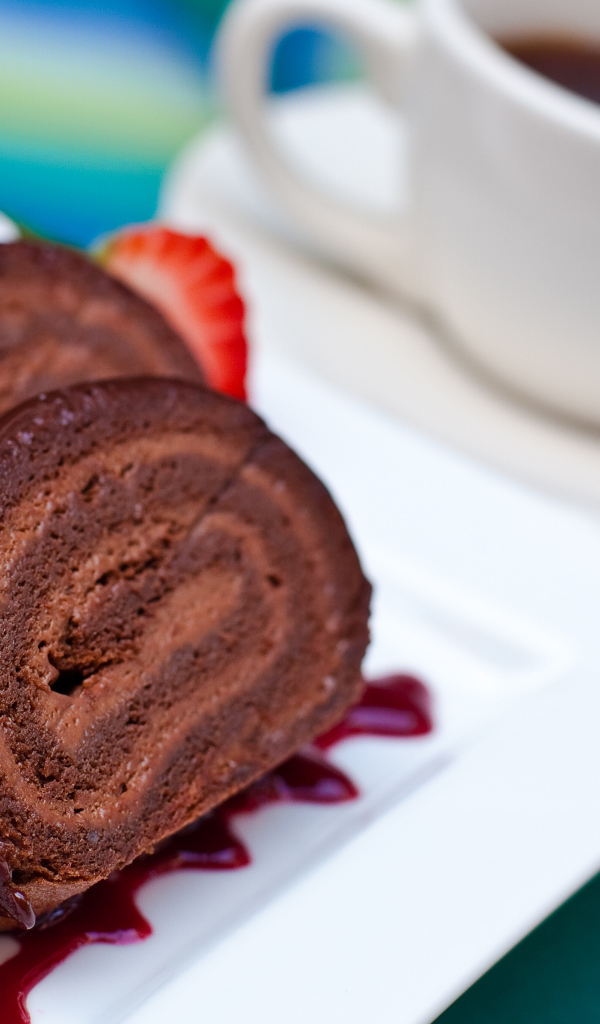 Сладкий рулет с клубничным джемом и чашкой чая на столе