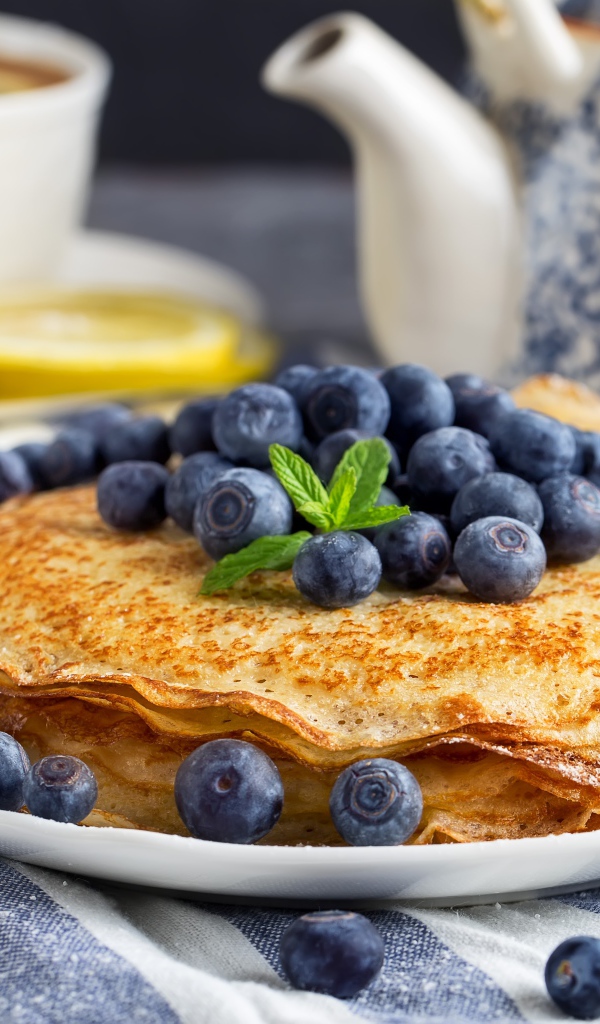 Тонкие блины с ягодами черники на столе с чаем