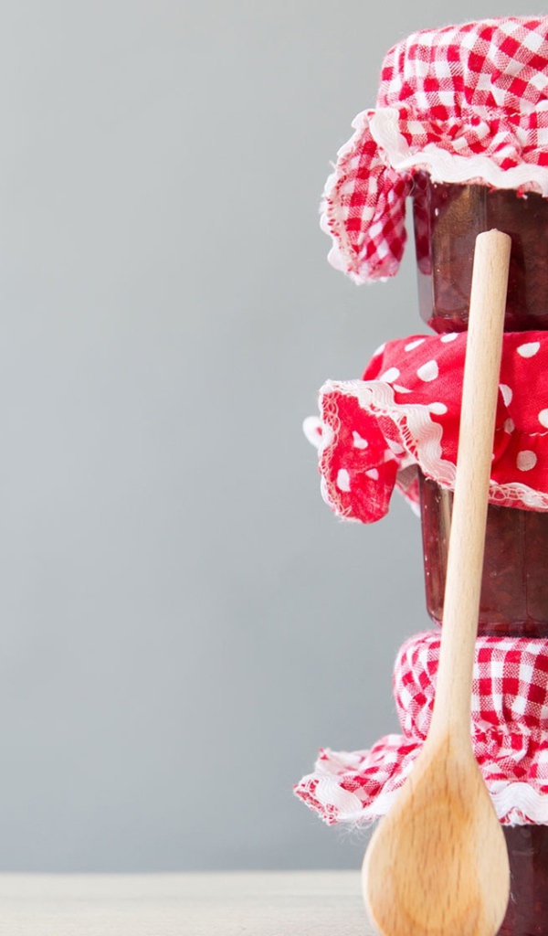 Три баночки варенья с деревянной ложкой на сером фоне