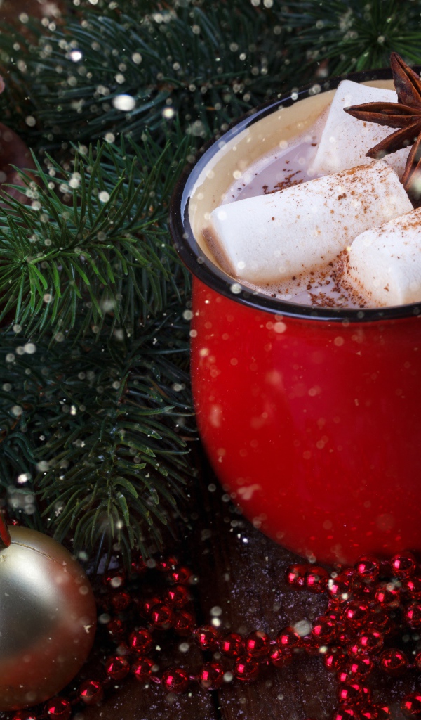 Чашка горячего какао с кусочками маршмеллоу и бадьяном на столе с еловой веткой 