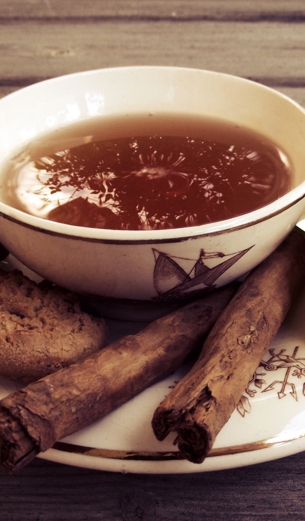 Чашка чая с печеньем, палочками корицы и цветами 