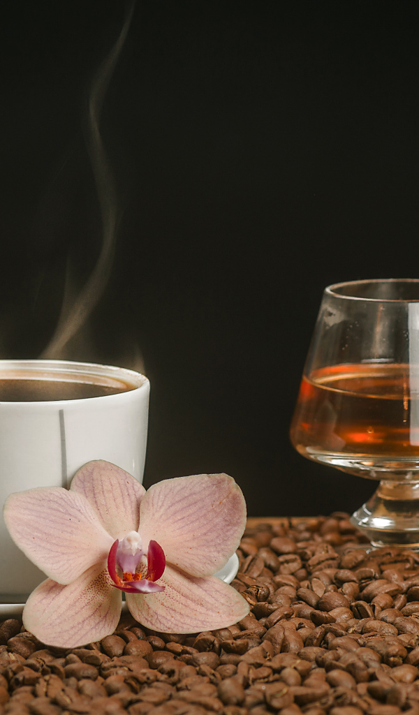 Ароматная чашка кофе на столе с бокалом виски, кофейными зернами и цветком орхидеи