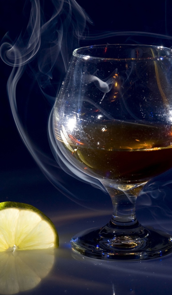 Бокал коньяка в дыму с кусочками лимона
