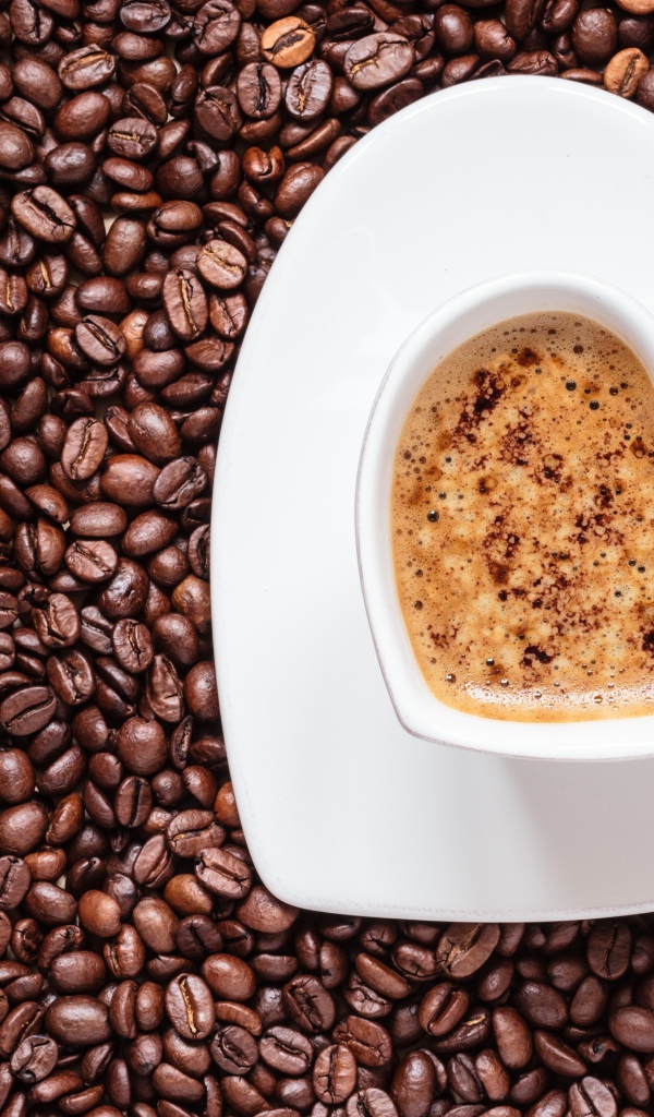 Белая чашка кофе в форме сердца стоит на кофейных зернах