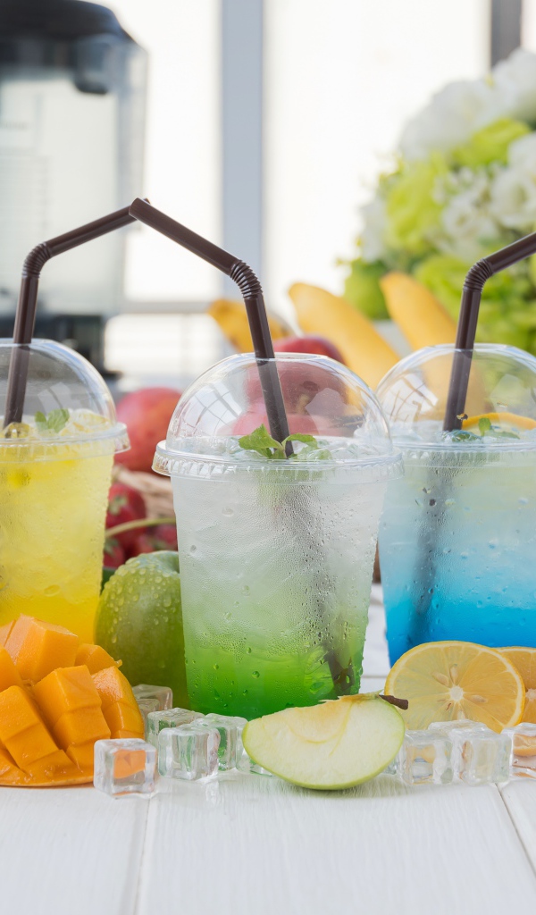 Коктейли в стаканах с трубочками на столе с кубиками льда и фруктами