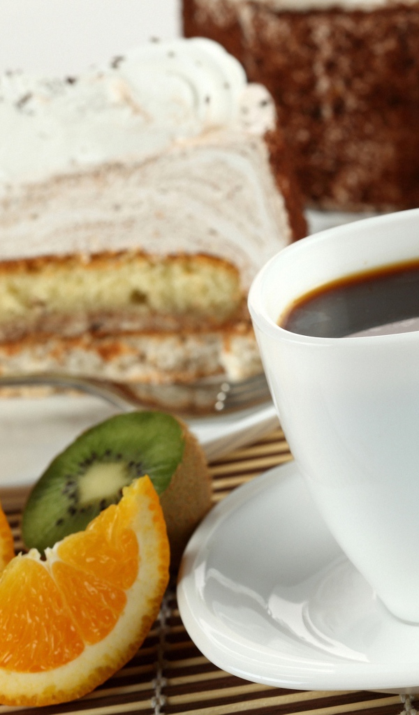Кофе с куском торта и кусочками апельсина и киви на столе