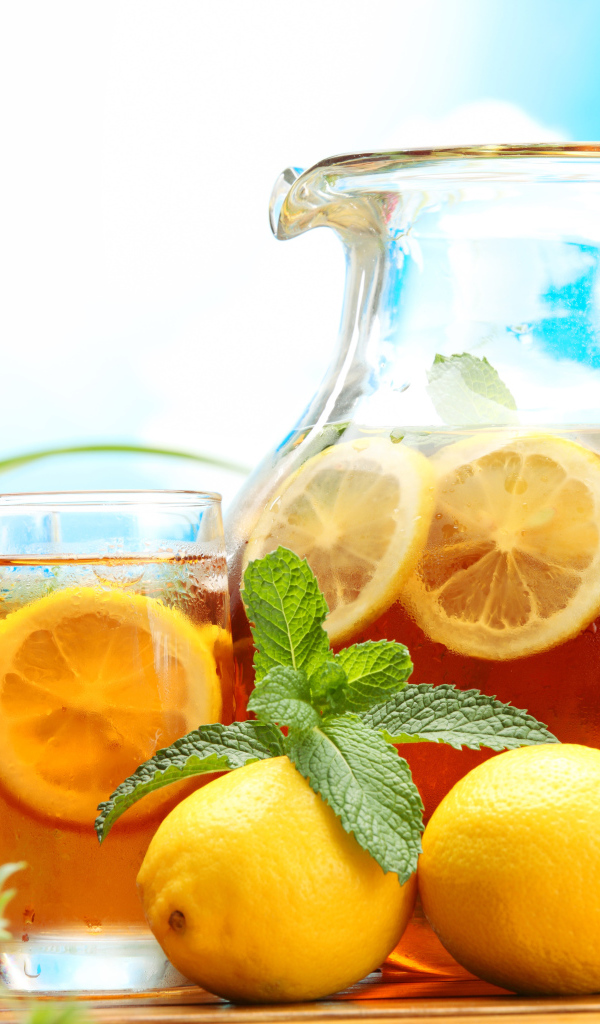 Холодный лимонад в графине на столе со стаканами и плодами лимона