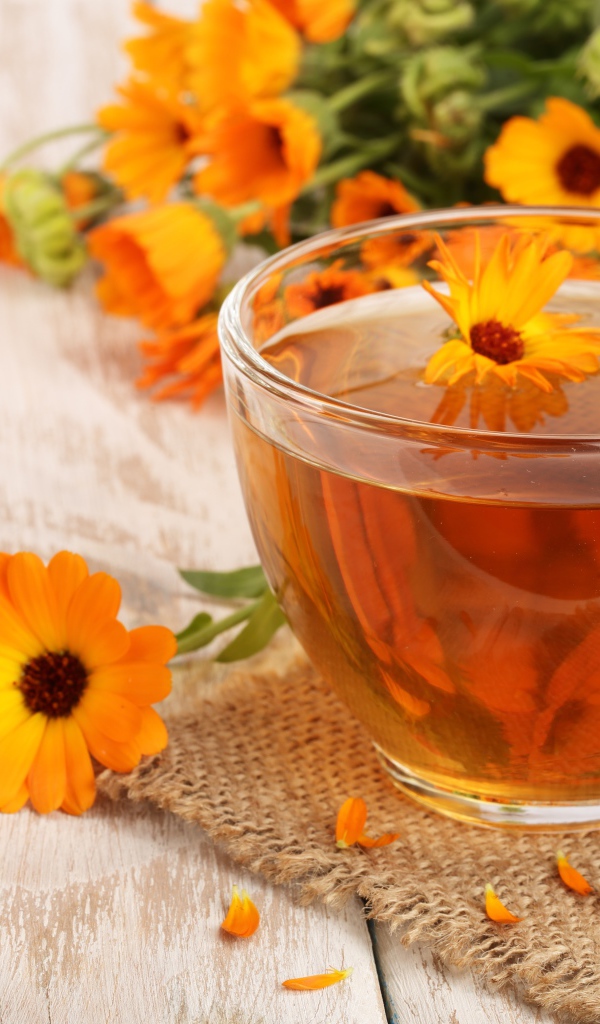 Стеклянная чашка чая с цветками календулы на столе
