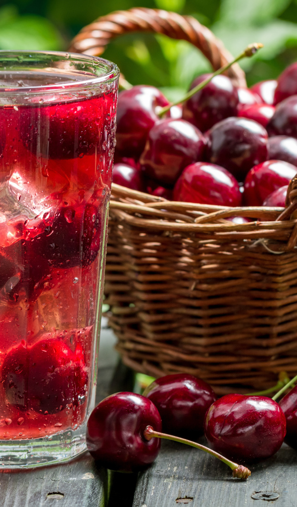 Стакан напитка со льдом на столе с корзиной с черешней 