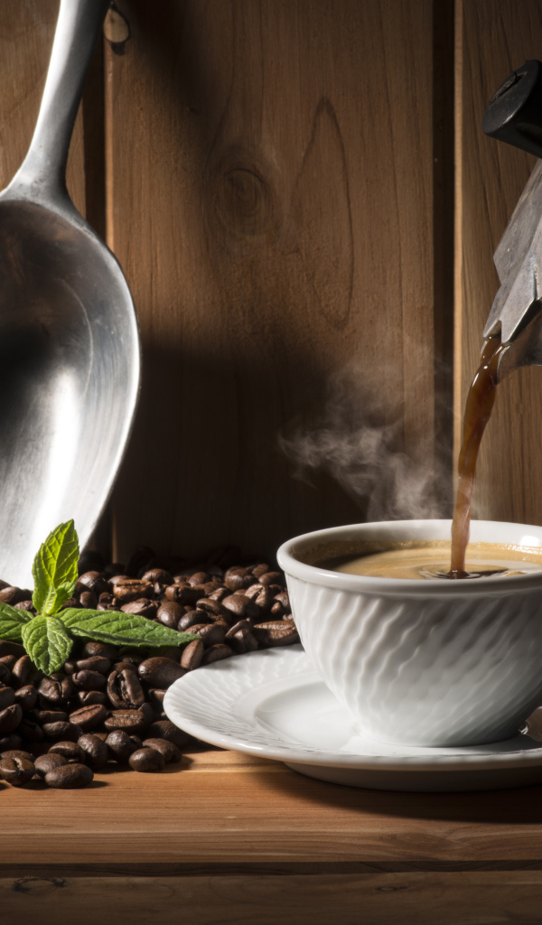 Горячий кофе наливают в чашку на столе с кофейными зернами