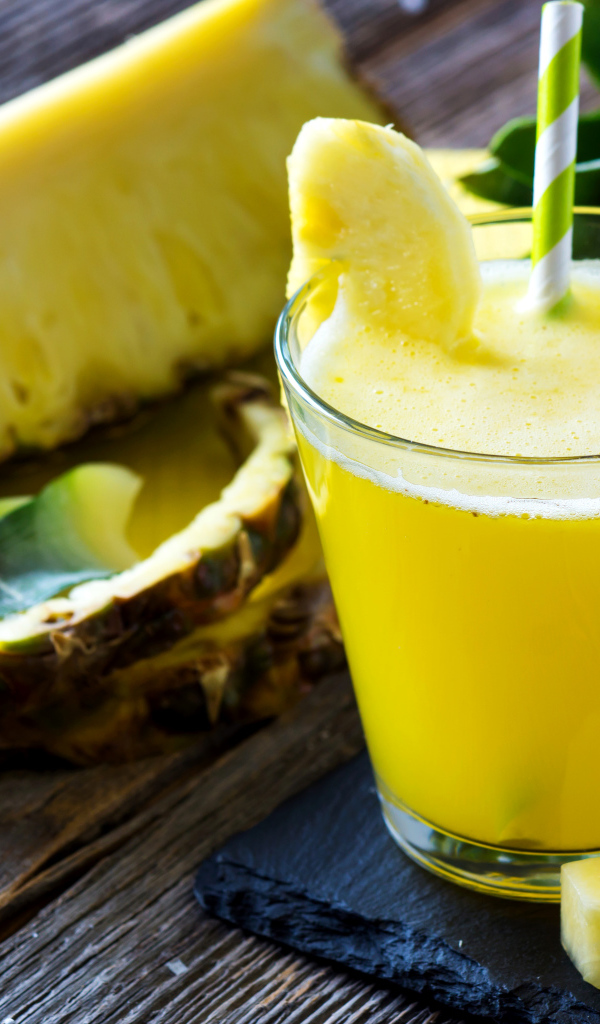 Ананасовый напиток в стакане на столе со свежими ананасами