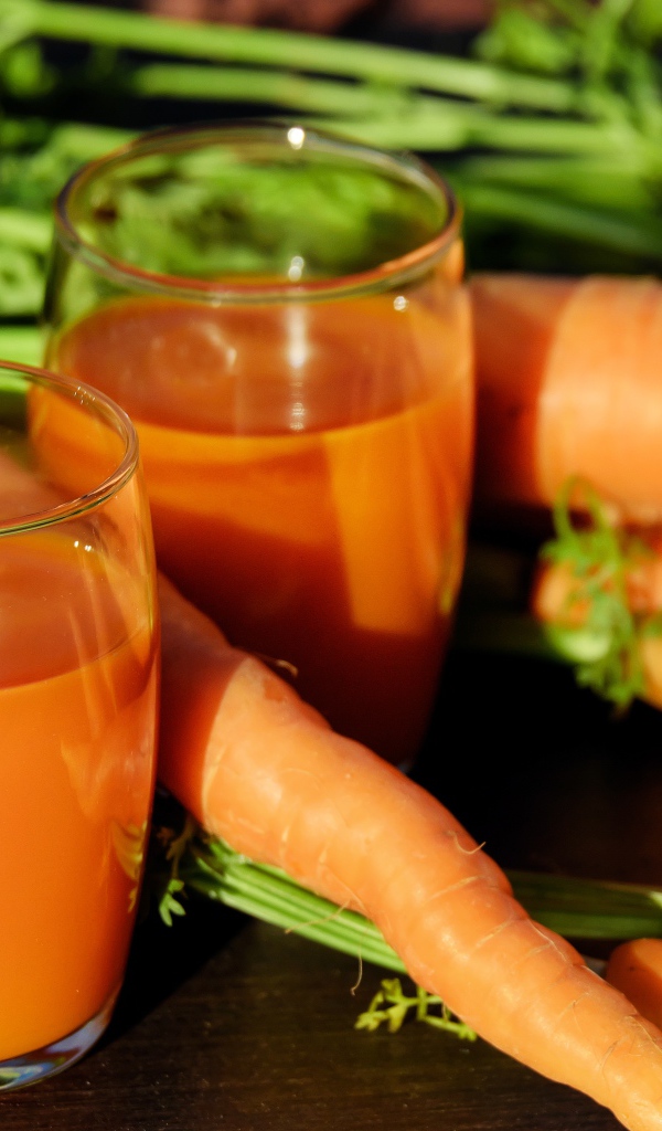 Два стакана морковного сока на столе со свежей морковью 