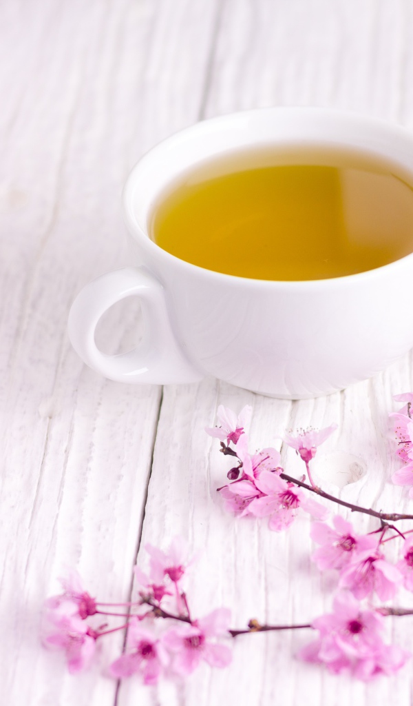 Белая чашка зеленого чая на столе с розовыми цветами