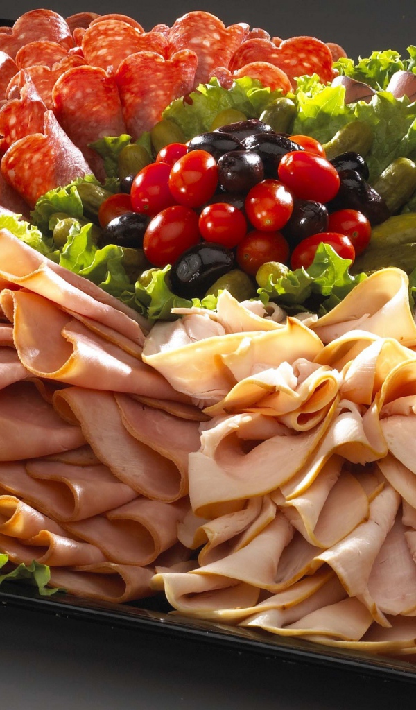 Большое блюдо с аппетитной мясной нарезкой, листьями салата и оливками