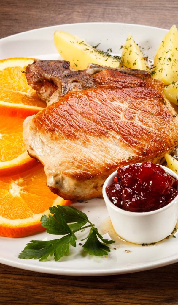 Кусок запеченного мяса с кусочками картофеля и апельсина и соусом