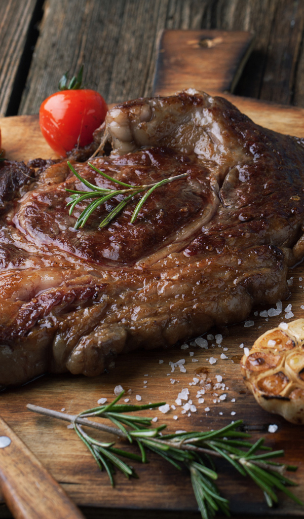 Кусок жареного мяса на разделочной доске с помидорами и чесноком