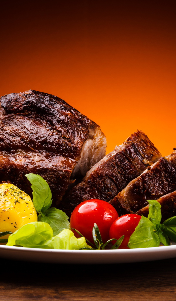 Кусок жареного мяса на тарелке с картофелем и помидорами 