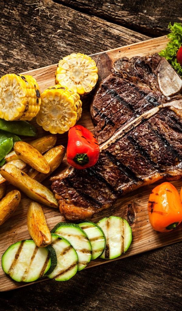 Кусок мяса на разделочной доске с овощами