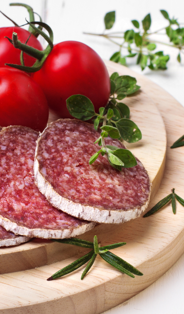 Вкусная колбаса на разделочной доске с помидорами и зеленью 