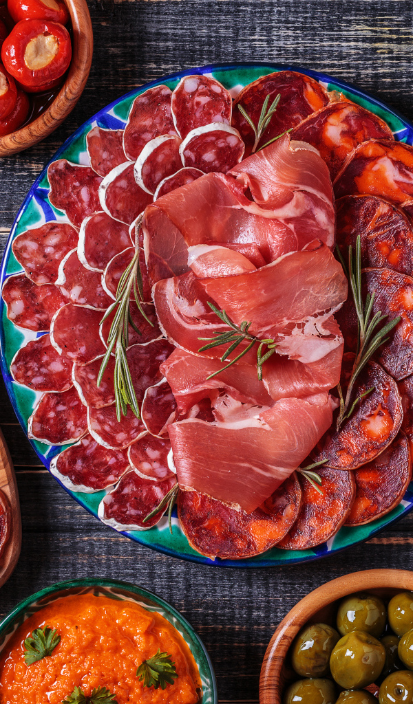 Большая тарелка с мясной нарезкой в центре праздничного стола