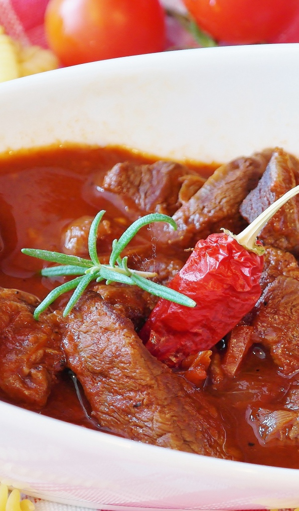 Мясной гуляш в белой тарелке с острым перцем