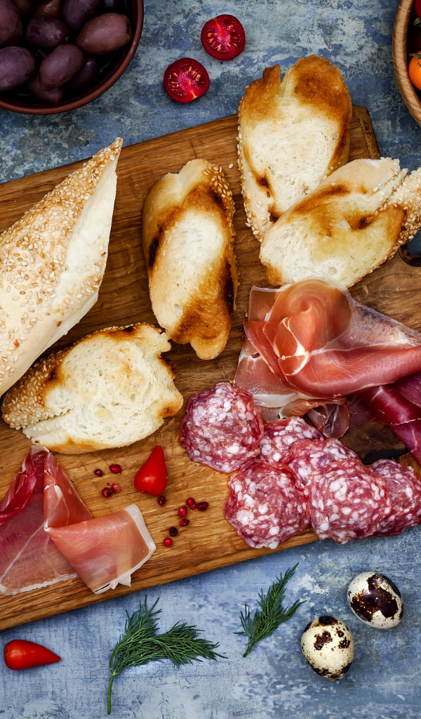 Мясные продукты с батоном и овощами на столе