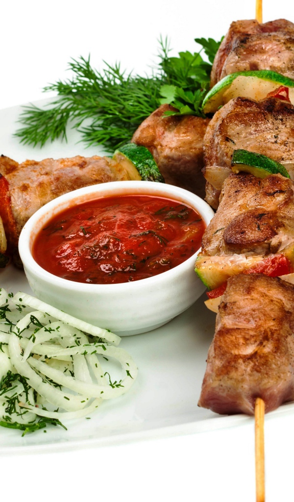 Шашлык на белой тарелке с соусом, зеленью и луком