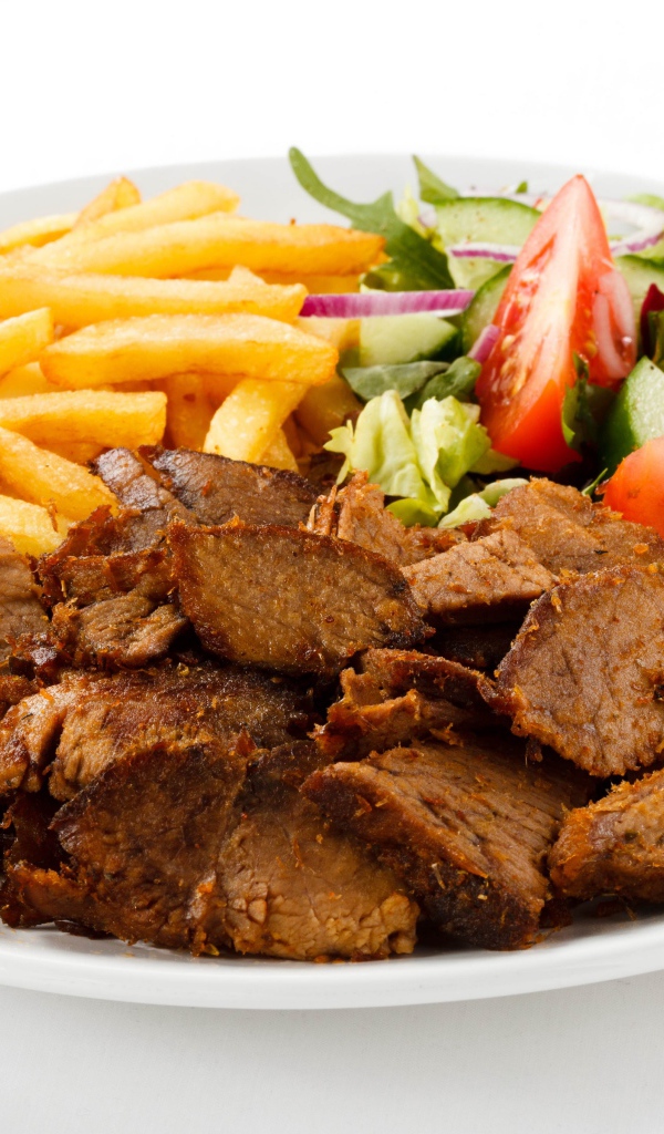 Кусочки мяса на тарелке с картофелем фри и салатом