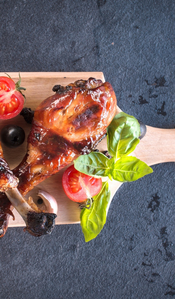 Две зажаренных куриных ножки с овощами на разделочной доске