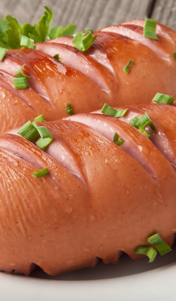 Два жареные сардельки на большой белой тарелке с зеленью 