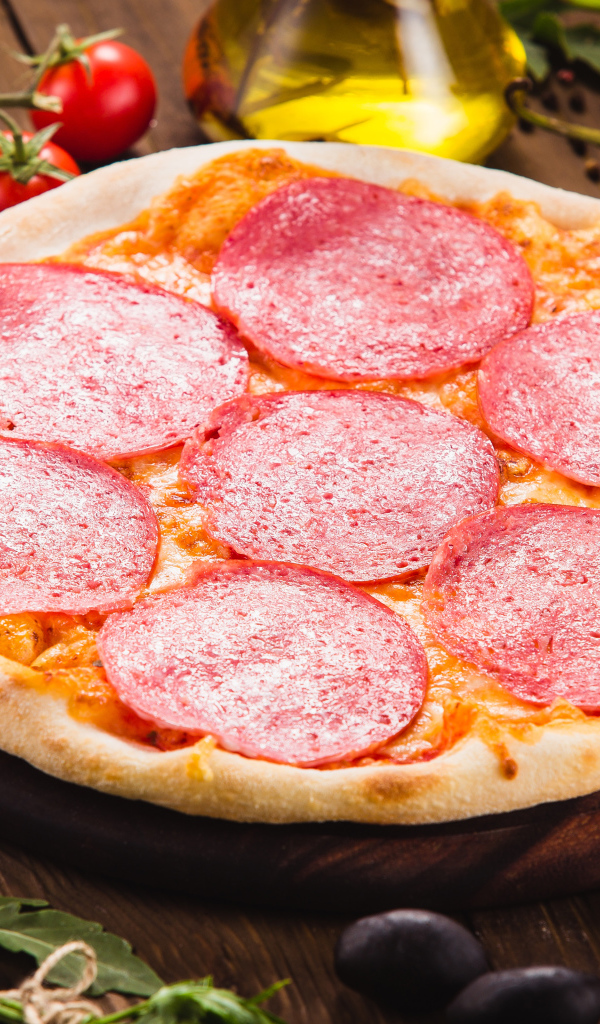 Пицца с салями на столе с овощами 