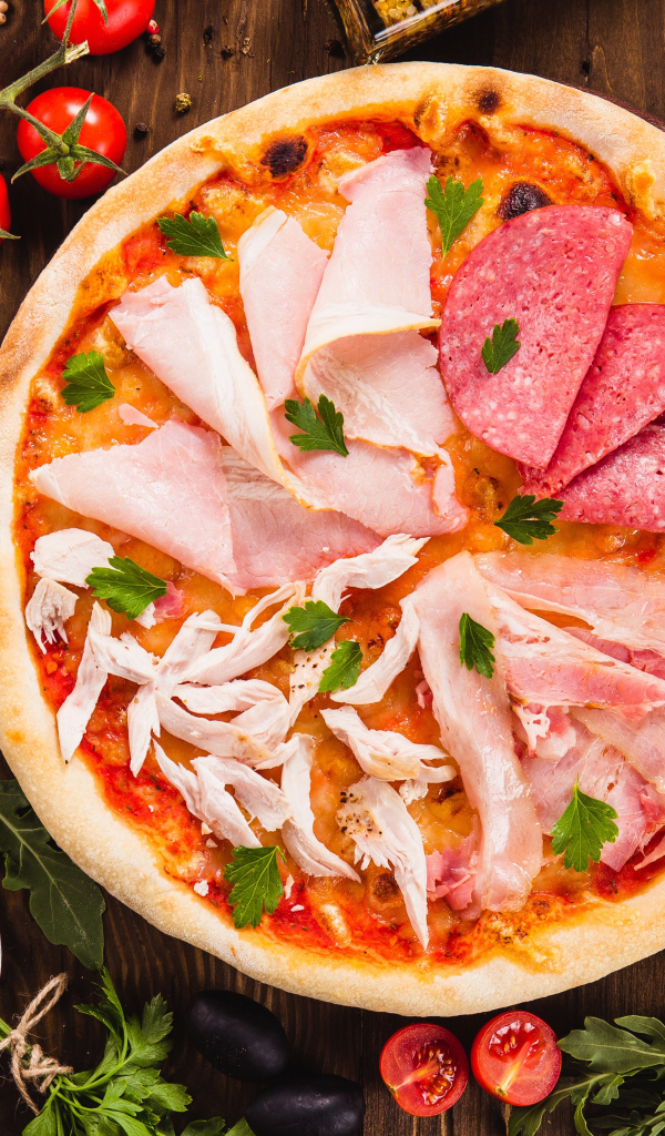 Пицца с колбасой, курицей и кусочками ветчины на столе с овощами 