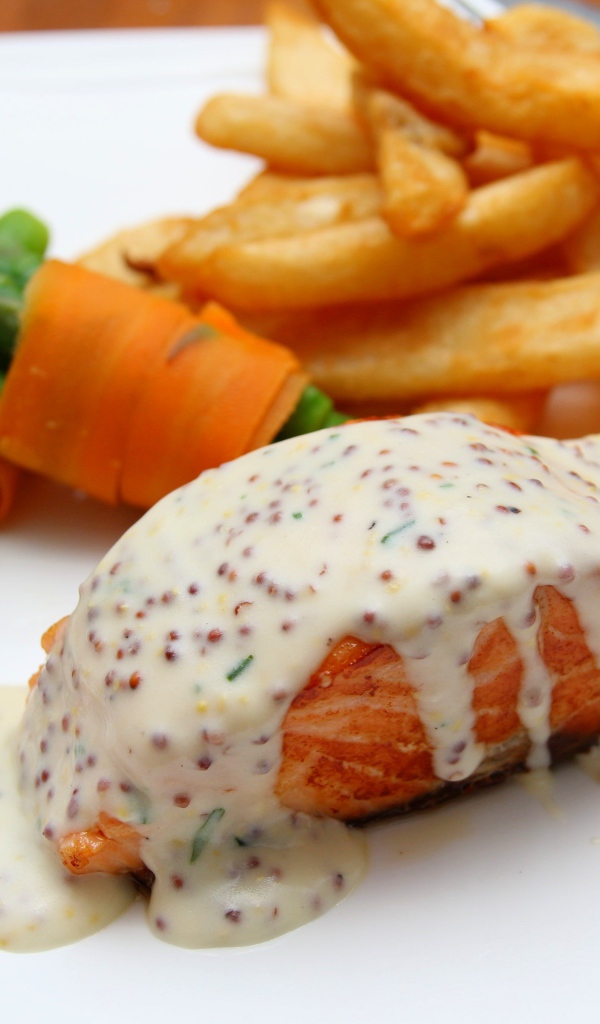 Кусок жареной красной рыбы с соусом на тарелке с картофелем фри 