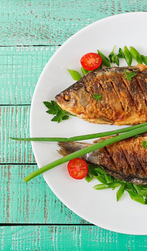 Жареная рыба с помидорами и зеленью на столе