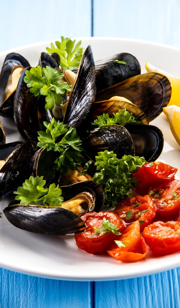 Мидии с томатами, кусочками лимона и зеленью петрушки на белой тарелке
