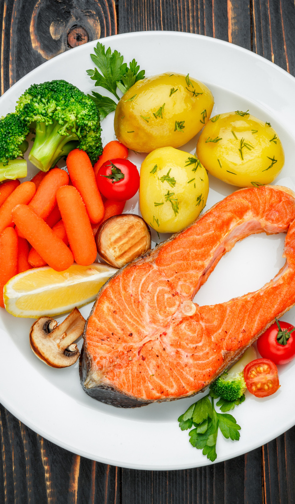 Красная рыба с овощами на белой тарелке на столе