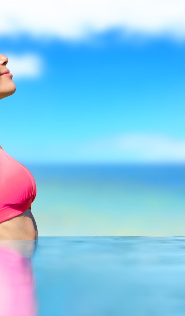 Девушка в розовом купальнике стоит в воде на солнце