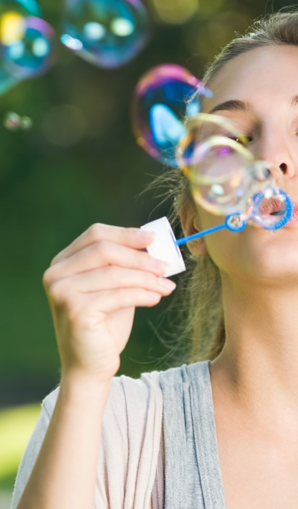 Милая молодая девушка пускает мыльные пузыри