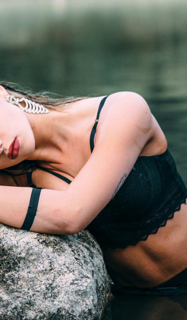 Молодая девушка с татуировками сидит у камня в воде