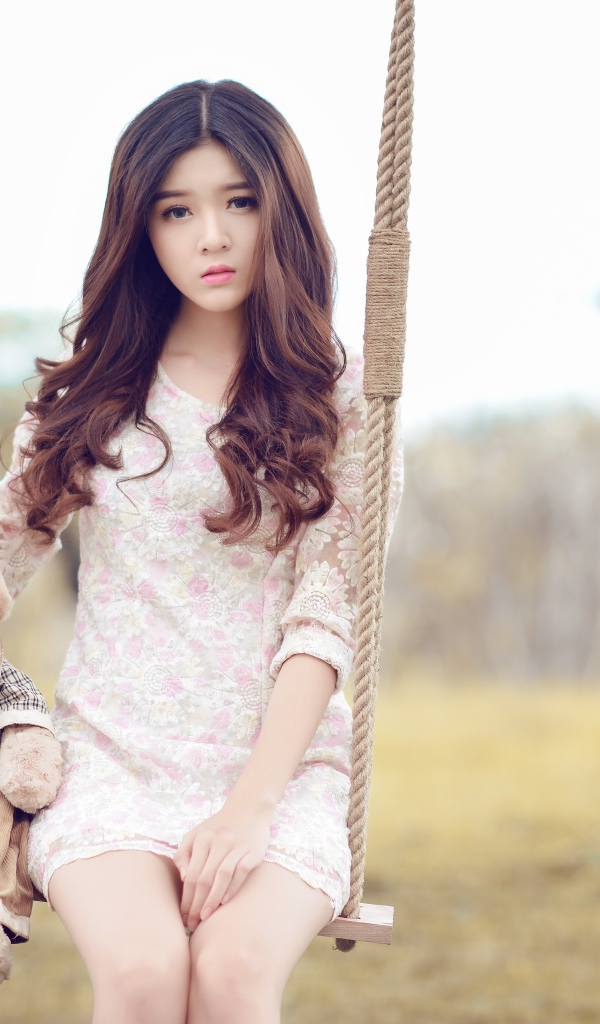 Девочка азиатка сидит на качели с плюшевым мишкой