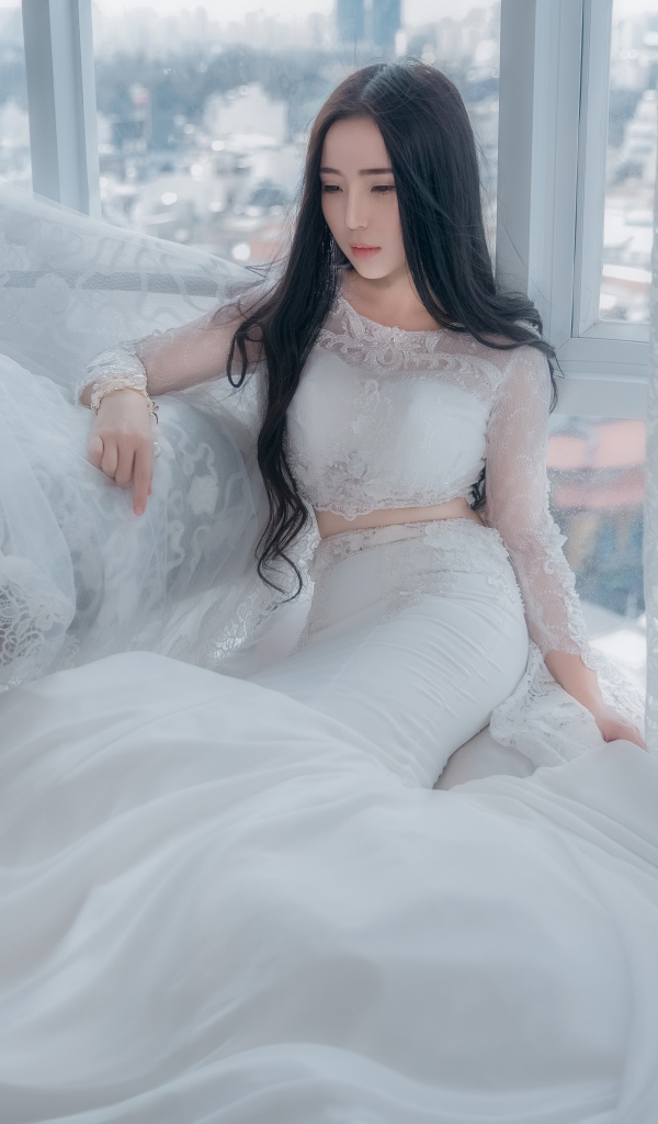 Красивая азиатка в белом свадебном платье сидит на полу