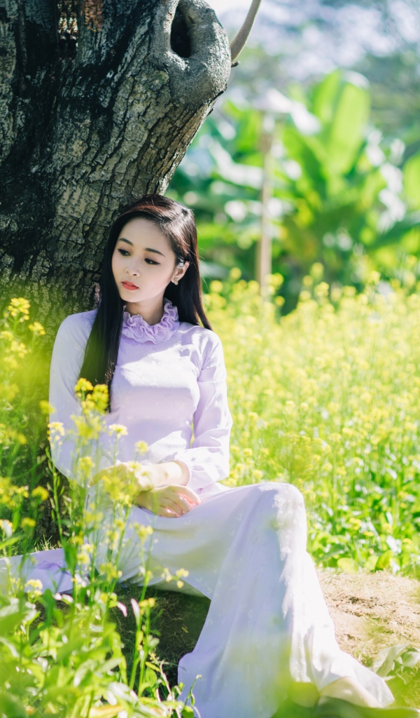 Красивая девушка азиатка сидит в белом платье под деревом