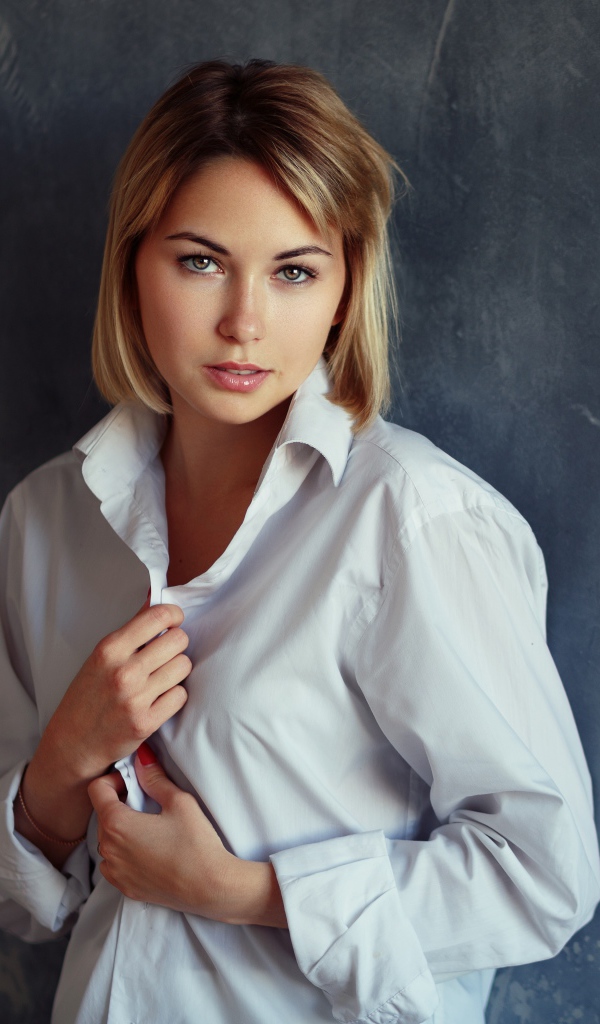 Красивая девушка блондинка в белой рубашке у стены 