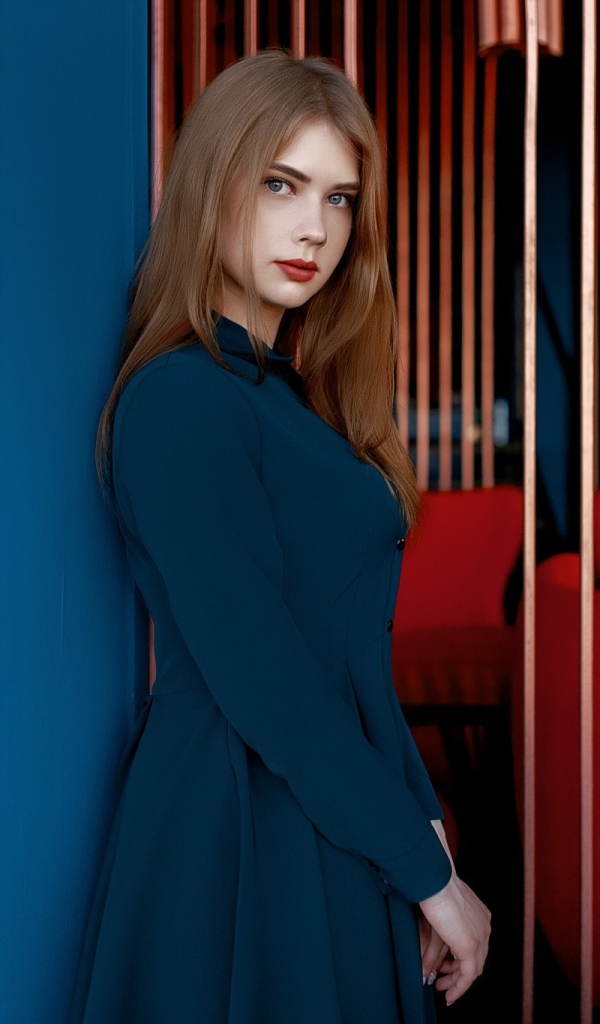 Красивая голубоглазая девушка стоит в пальто у стены