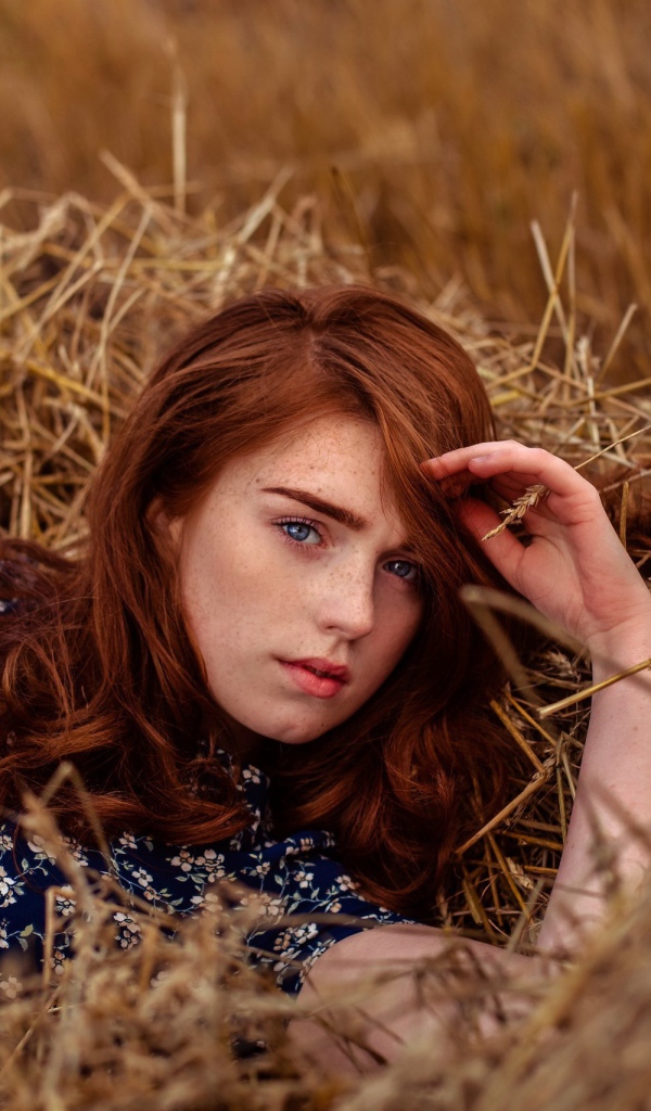 Красивая голубоглазая рыжеволосая девушка лежит в сене