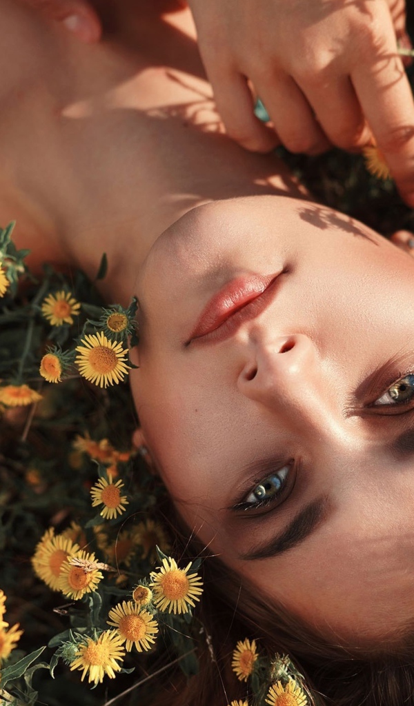Красивая шатенка лежит на земле с желтыми цветами